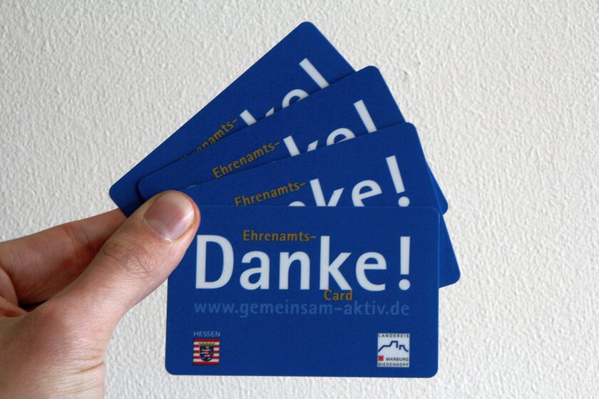 Vier Ehrenamtscards zwischen Daumen und Zeigefinger gehalten